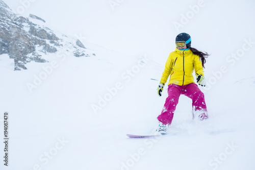 Picture of female athlete wearing helmet with developing hair, snowboarding from mountain slope