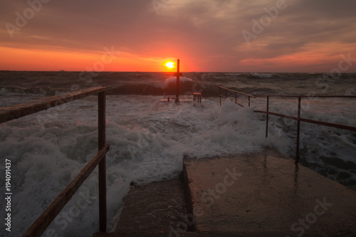 beautiful sea landscape in sunrise time, colorful pink and orange sky and storm in the sea. Old concrete pier © serejkakovalev