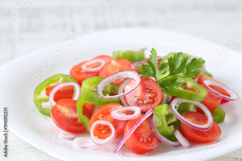 Healthy, fresh and delicious vegetable salad with cherry tomatoes, red onion rings, green pepper rings, parsley and olive oil