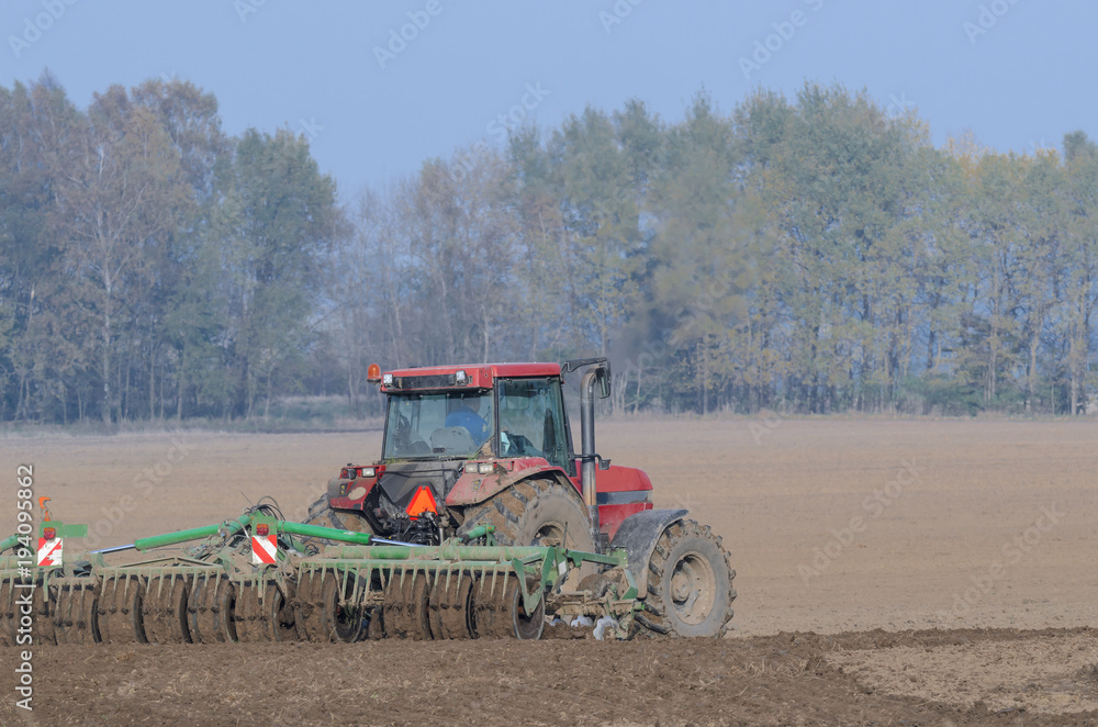 Obraz premium FARM - Tractor while working on a plowed field