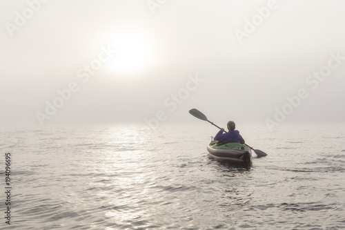 Girl kayaking on an inflatable kayak in Howe Sound during a fog covered winter sunset. Taken in West Vancouver, BC, Canada.
