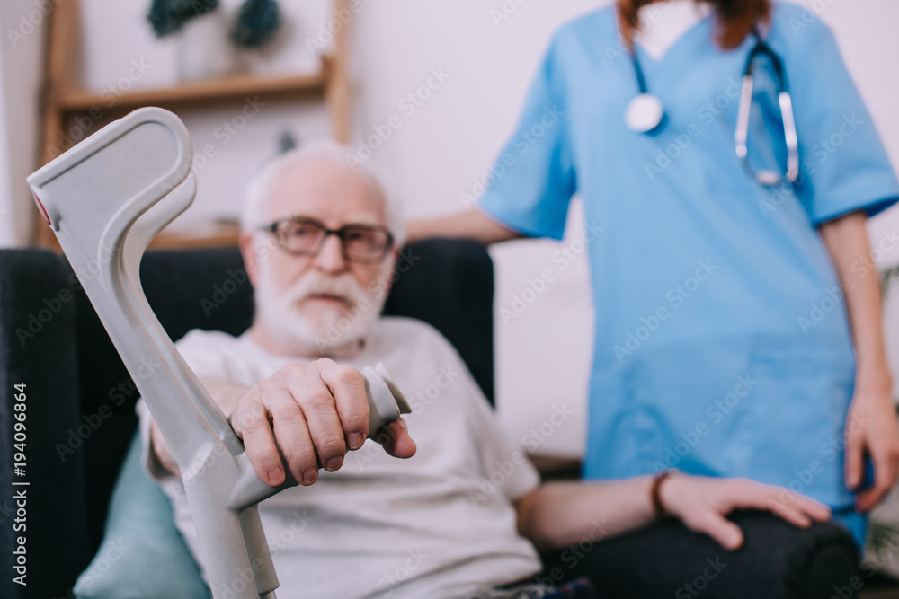Obraz premium Nurse standing behind senior man with crutch
