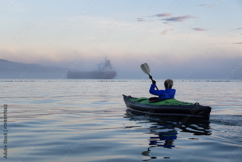 Adventure girl is kayaking on an inflatable kayak in Horseshoe Bay with a ship in the background. Taken in Vancouver, BC, Canada, during a winter sunset.