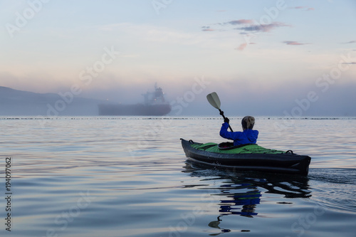 Adventure girl is kayaking on an inflatable kayak in Horseshoe Bay with a ship in the background. Taken in Vancouver, BC, Canada, during a winter sunset. © edb3_16