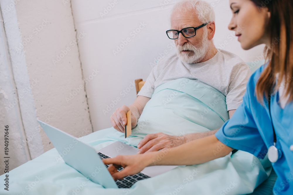 Obraz premium Nurse helping senior patient using laptop and credit card