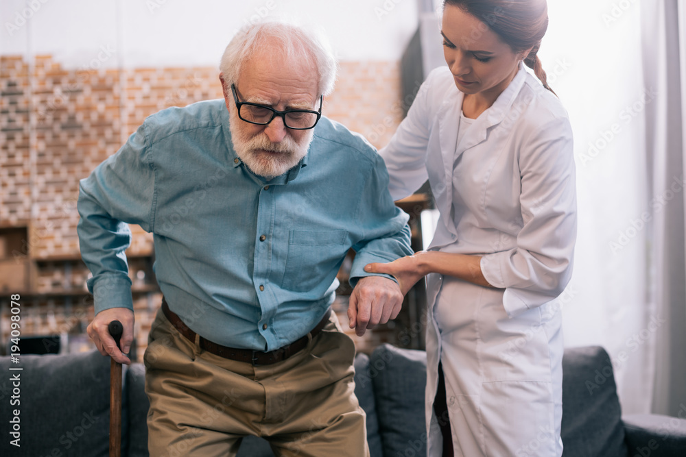 Obraz premium Old man leaning on cane and female doctor hand