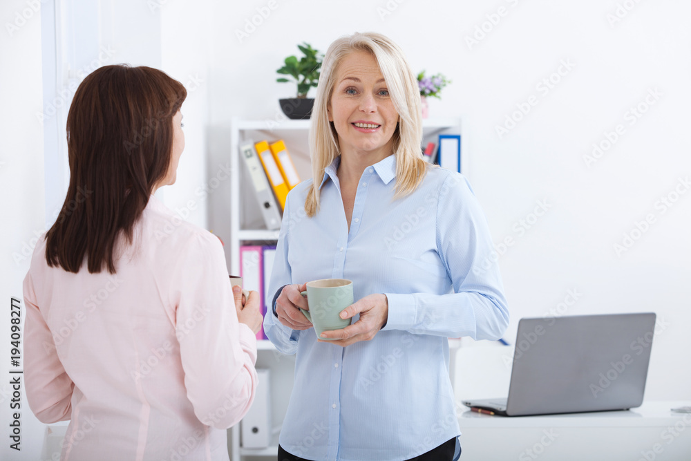 Office coffee break. Two female colleagues with cups of coffee talking. Office coffee break. Two female colleagues with cups of coffee talking.