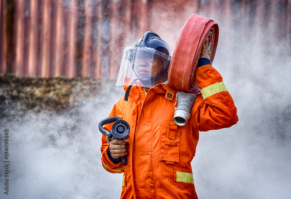 Obraz premium Emergency Fire Rescue training, firefighters in uniform, carry a water hose run through flame