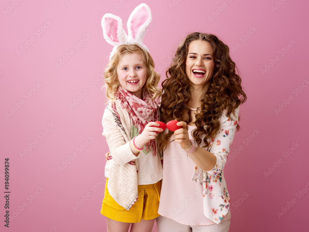 mother and daughter red Easter eggs tapping isolated on pink