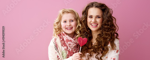 smiling stylish mother and child holding heart shaped lollipop
