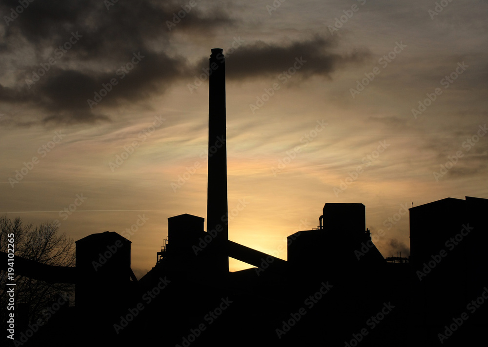 Factory chimney and buildings against evening sun.