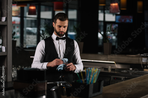 handsome bartender cleaning glass with rag in evening