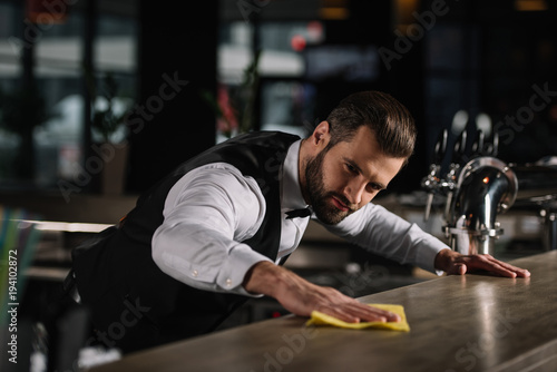 handsome bartender cleaning bar counter in pub