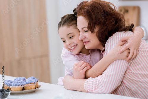 embracing grandmother and little granddaughter looking at creamy cupcakes