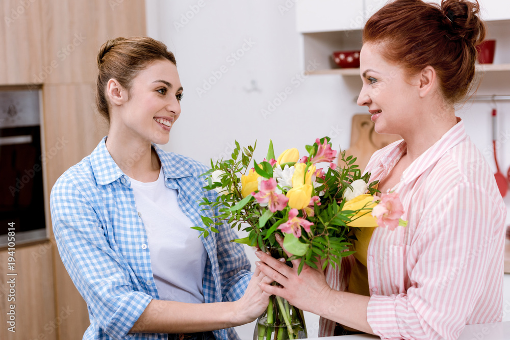 young woman presenting beautiful bouquet to her mother for mothers day young woman presenting beautiful bouquet to her mother for mothers day