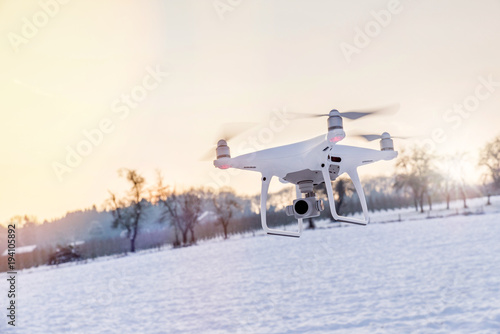 White drone camera floating in air with white snow and field in background