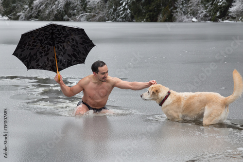 Bizarre picture of a man holiding an umbrella and petting a dog in a frozen lake. Taken in Alice Lake, Squamish, North of Vacouver, BC, Canada. photo