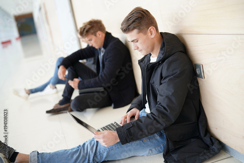 Students in corridor websurfing with laptop