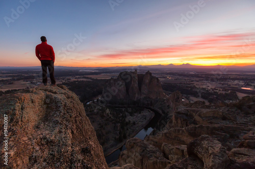 Man standing on top of a mountain is enjoying a beautiful landscape during a colorful and vibrant sunset. Taken at Smith Rock, Oregon, North America. © edb3_16