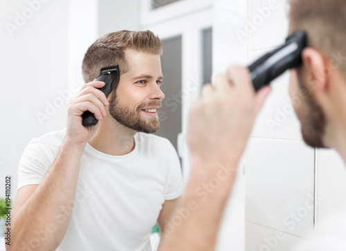 Handsome man cutting his own hair with a clipper photo