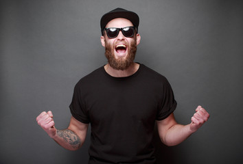 Hipster handsome male model with beard wearing black blank t-shirt with space for your logo or design over gray background