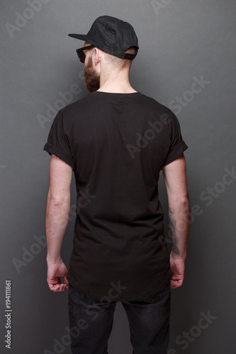 Hipster handsome male model with beard wearing black blank t-shirt with space for your logo or design over gray background © 4Max