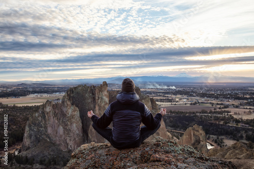 Adventurous man sitting in a meditation pose on top of a cliff during a vibrant sunset. Taken in Smith Rock, Oregon, America. Concept: adventure, freedom, travel, holiday, vacation