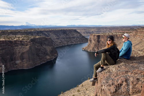 Friends sitting at the edge of a cliff and enjoying the beautiful landscape. Taken at The Cove Palisades State Park in Oregon, North America.