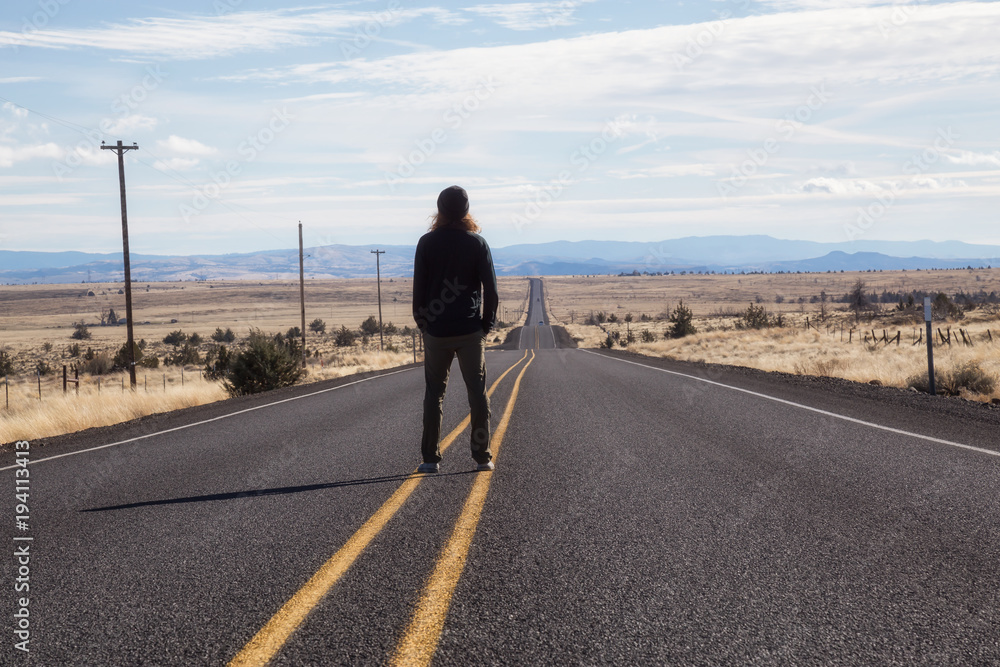 Man is standing in the middle of the long road during a vibrant sunny day. Taken in Oregon, North America.
