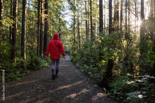 Girl wearing a bright red jacket is walking the the beautiful woods during a vibrant winter morning. Taken in Ucluelet, Vancouver Island, BC, Canada.