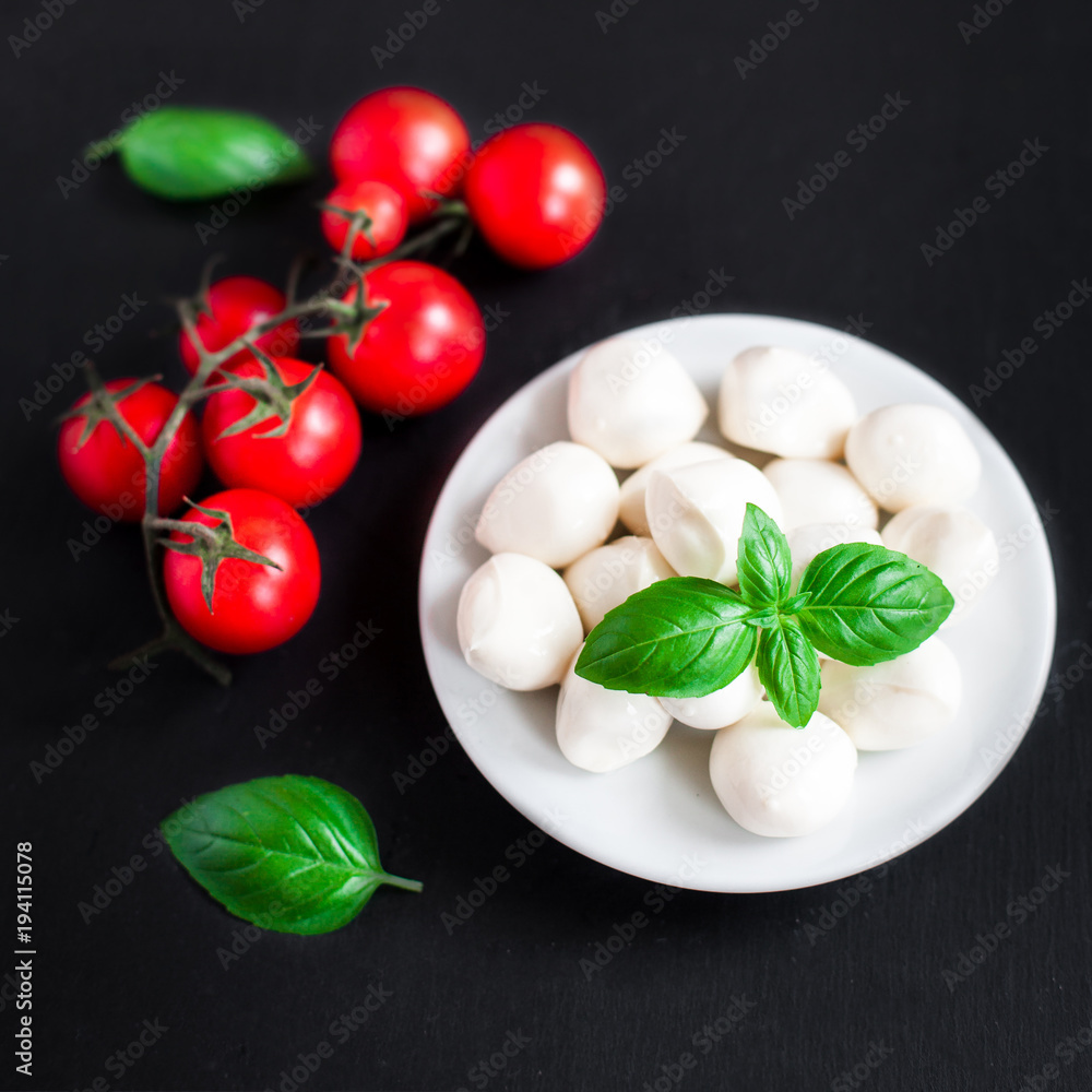 Fresh cherry tomatoes, basil leaf, mozzarella cheese on black slate stone chalkboard with copyspace. Healthy Italian traditional caprese salad ingredients. Organic Mediterranean food concept, flat lay Fresh cherry tomatoes, basil leaf, mozzarella cheese on black slate stone chalkboard with copyspace. Healthy Italian traditional caprese salad ingredients. Organic Mediterranean food concept, flat lay