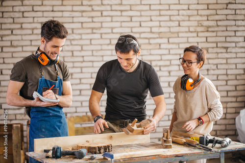 Fotografija young carpenter with students in woodworking workshop show how working with plan