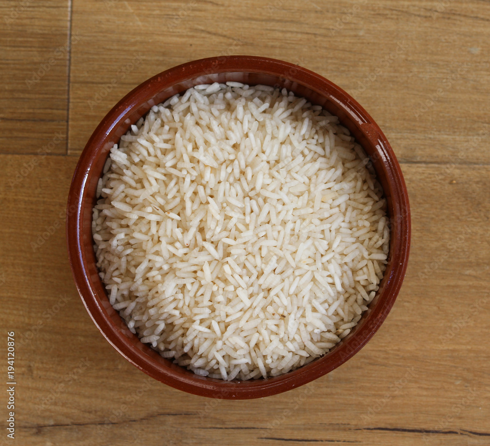 Stone bowl with uncooked white rice on wooden background Stone bowl with uncooked white rice on wooden background
