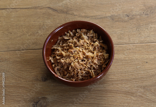 Stone bowl with fried onions on wooden background