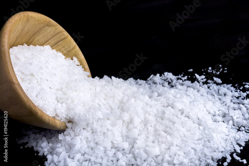 Sea salt white crystals in wooden bowl isolated on the dark background.