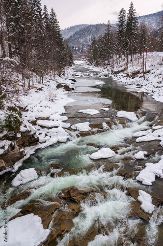Winter landscape. Mountain river flows from the rocks. Snow and mountain river