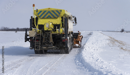 snow-clearing truck on the road sprinkles aggregate and salt