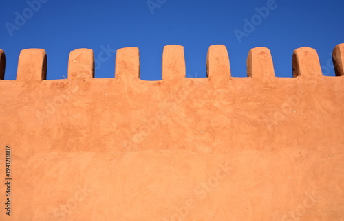 Pięknie wykończony zabytkowy mur w kolorze brzoskwiniowym w stylu arabskim, w tle piękny błękit nieba