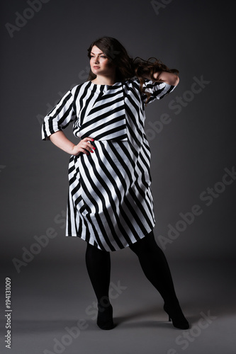Plus size fashion model in striped dress, fat woman on gray background, overweight female body