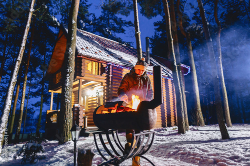 A man fries grilled meat against the background of the cottage in the evening and in the smoke