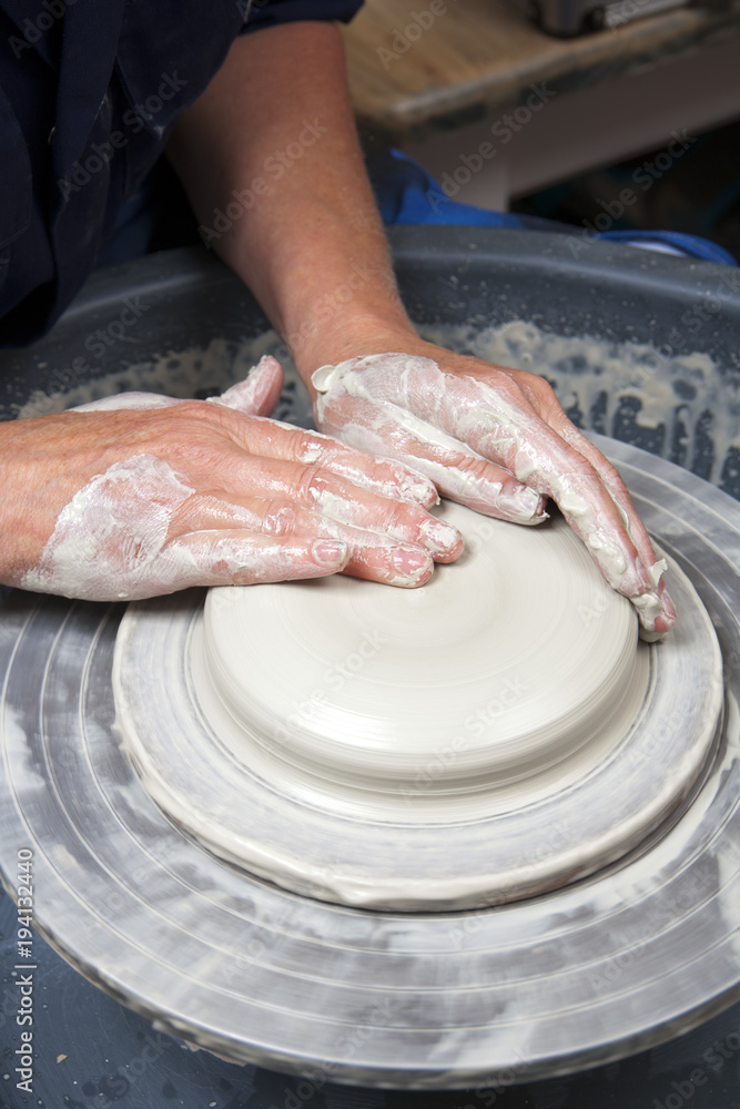 A lady ceramics artist at work in her home pottery studio, throwing a bowl on a wheel. Opening up.