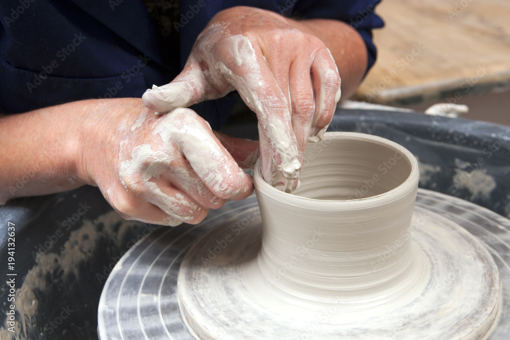 A lady ceramics artist at work in her home pottery studio, forming a mug shape