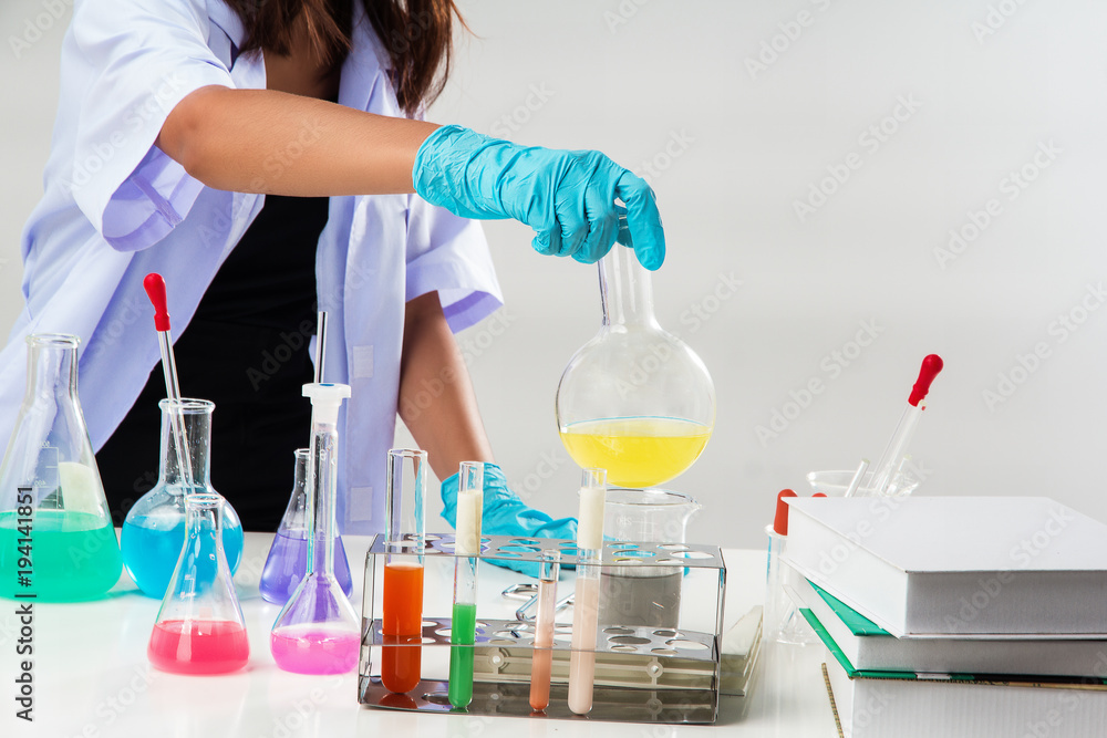 Fototapeta premium The lady in white uniform with blue rubber glove, The chemist is working by test tube with reagent in lab