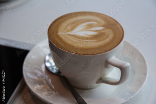 In selective of heart picture from cream foam of cuppuccino coffee cup put on table and coffee shop,blurry light around. photo