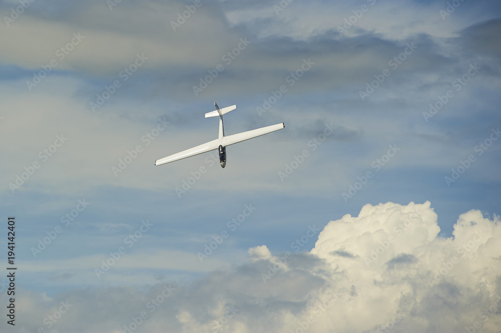 Obraz premium A Glider flying in blue sky with big white clouds. The glider is a plane that has no engine 