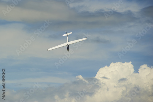 A Glider flying in blue sky with big white clouds. The glider is a plane that has no engine 