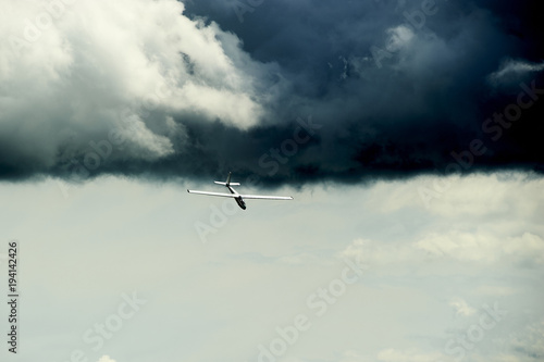 A Glider flying away from storm. The glider is a plane that has no engine.
