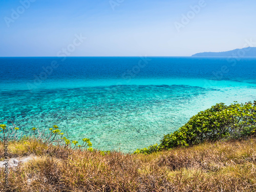 Wonderful seascape. Clear blue sky and turquoise sea and coral reef with green plants on the hill.