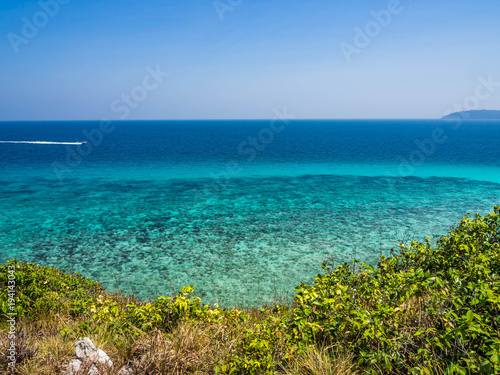 Wonderful seascape. Clear blue sky and turquoise sea and coral reef with green plants on the hill.