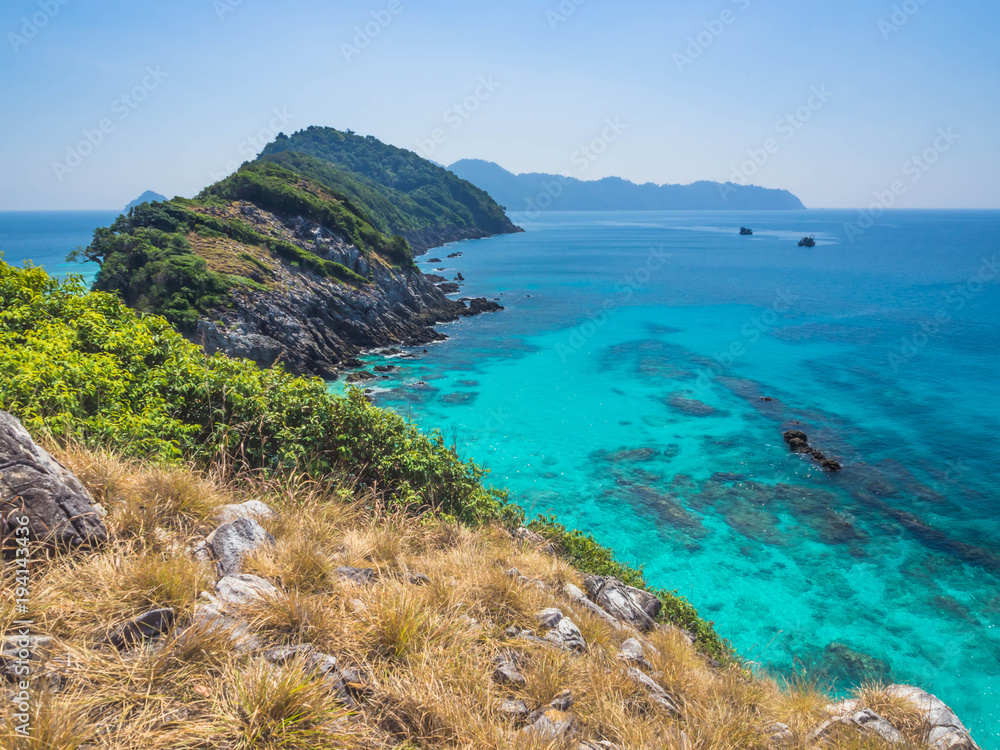 Wonderful landscape of clear and clean turquoise sea with two boats and dry grass on the hill.